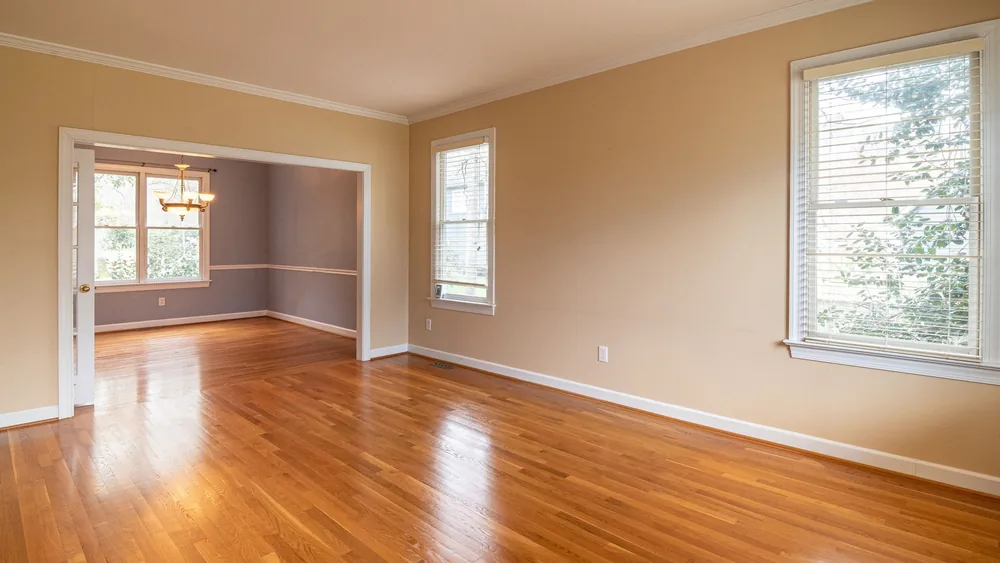 Bright empty room with wooden floors and large windows, ideal for real estate listings.