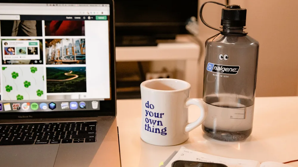 Cozy workspace with laptop, motivational mug, and water bottle, perfect for remote work inspiration.