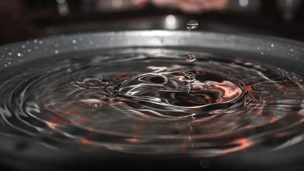 A detailed macro shot of water droplets creating ripples on a reflective surface, showcasing fluid dynamics.