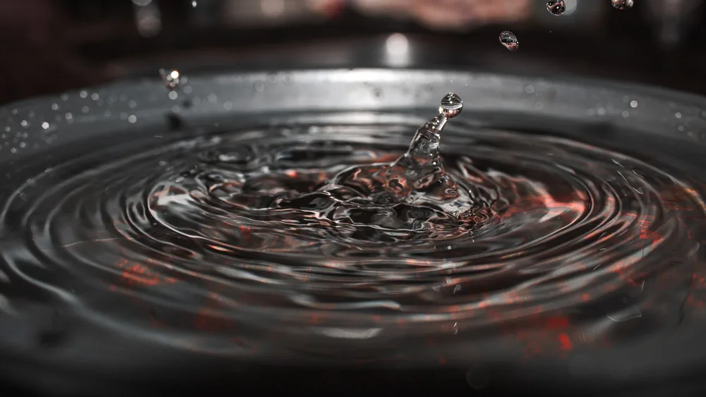 Close-up of a water droplet creating ripples in a dark, reflective surface.