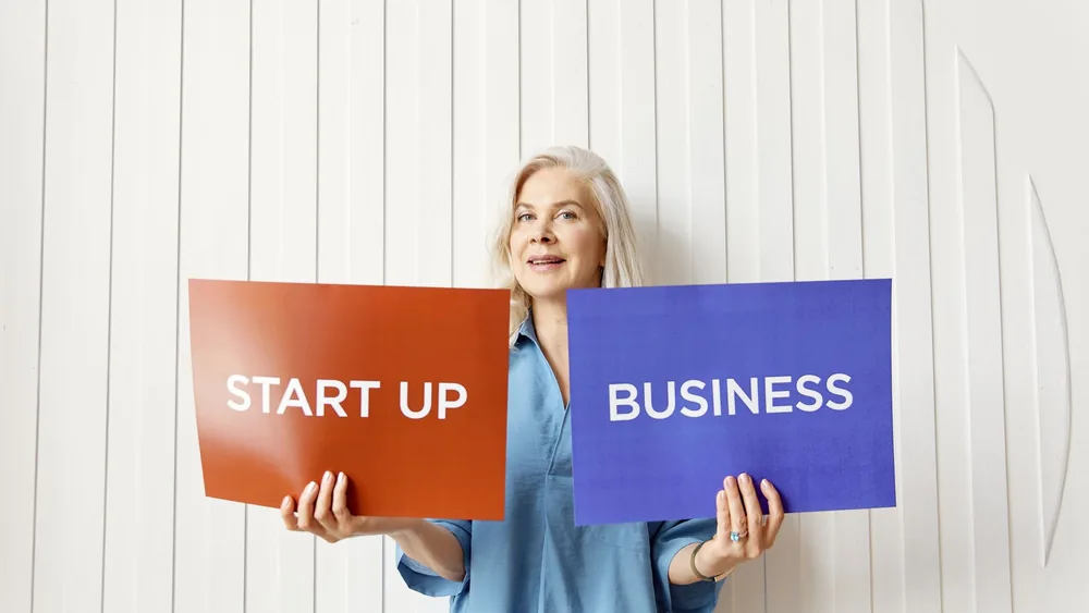Elderly woman holding startup and business signs indoors against white background.