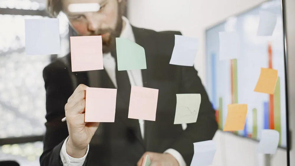 Professional man utilizes sticky notes on glass for planning in an office setting.