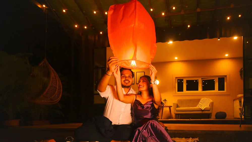 Couple releasing lantern in a cozy outdoor setting with warm lighting, capturing a romantic moment.