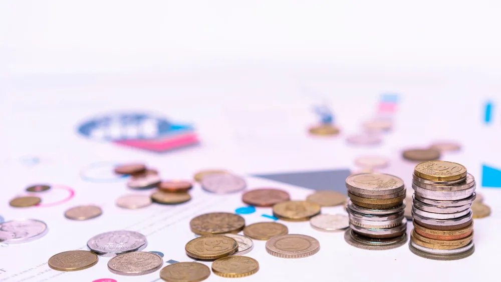 Stack of assorted coins with financial documents on a white background, highlighting the concept of savings.