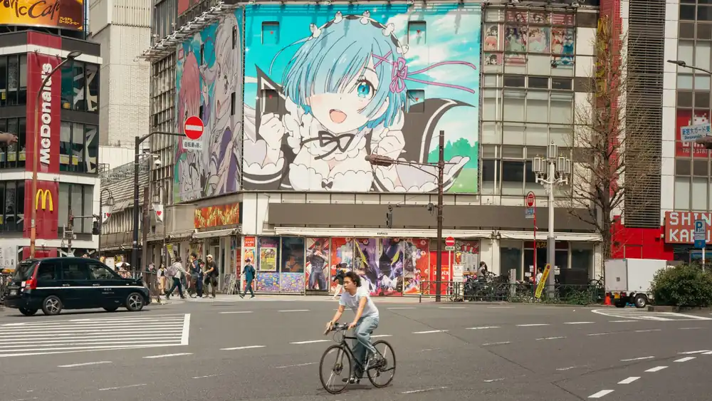 Street scene in Tokyo with anime billboard and cyclist crossing.