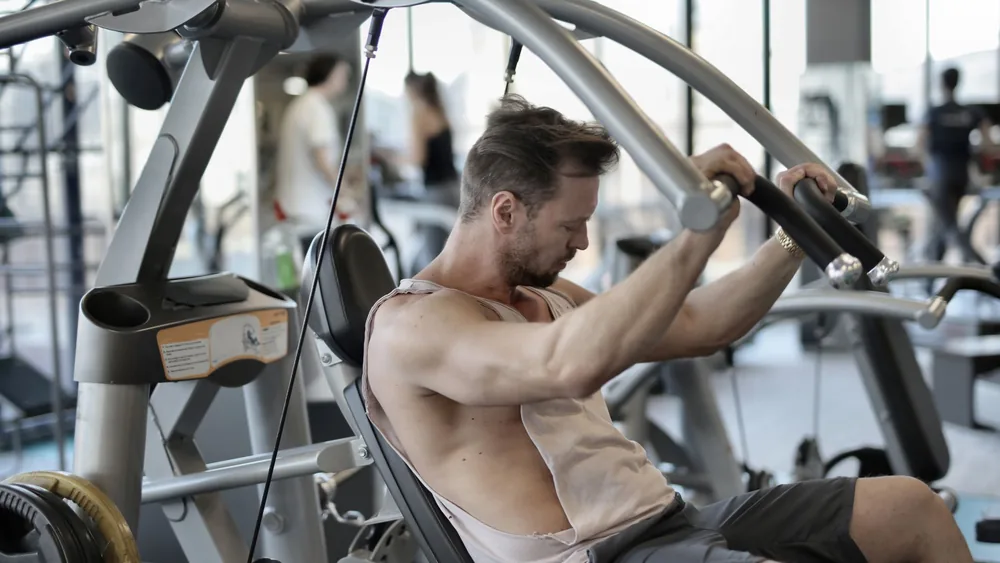 Side view of concentrated male athlete in sportswear pumping muscles during training in fitness center and using shoulder press machine