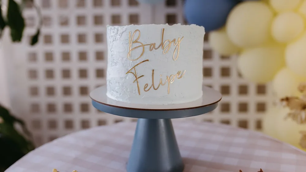 White cake with Baby Felipe inscription surrounded by pastel balloons at a baby shower.