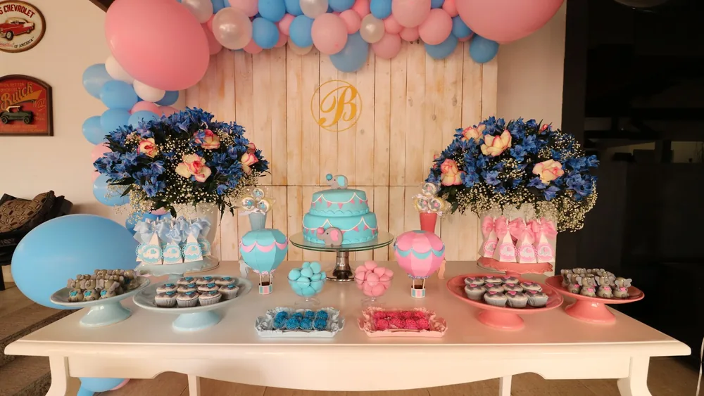 Vibrant dessert table decorated with blue and pink balloons, flowers, and sweets for a baby shower.