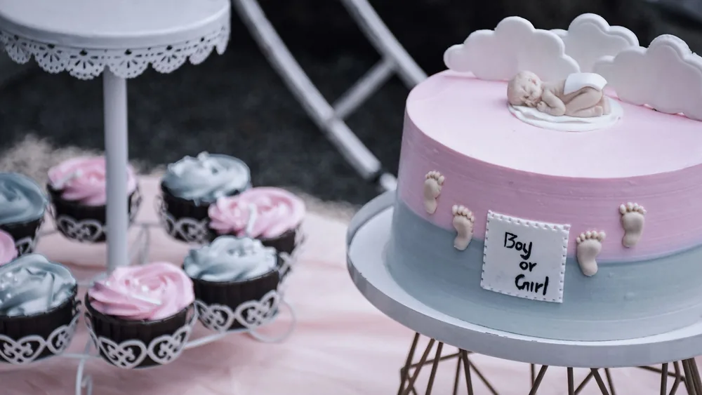 A gender reveal cake with baby decor and pink and blue cupcakes on a stand, perfect for celebrations.