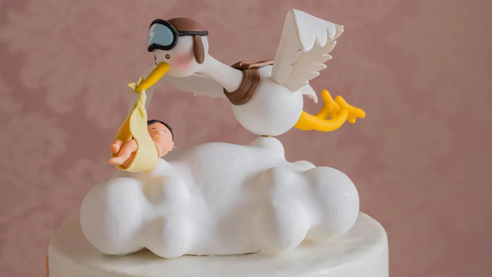 Close-up of a whimsical stork carrying a baby figurine on a cake top, ideal for baby showers.
