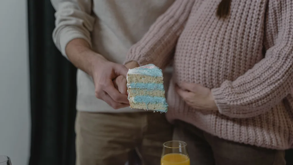 A pregnant couple revealing their baby's gender with a slice of blue cake.
