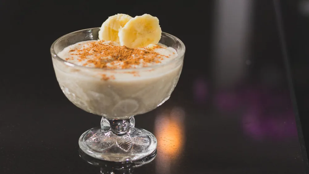 Creamy banana dessert topped with cinnamon served in a stemware on a reflective surface.