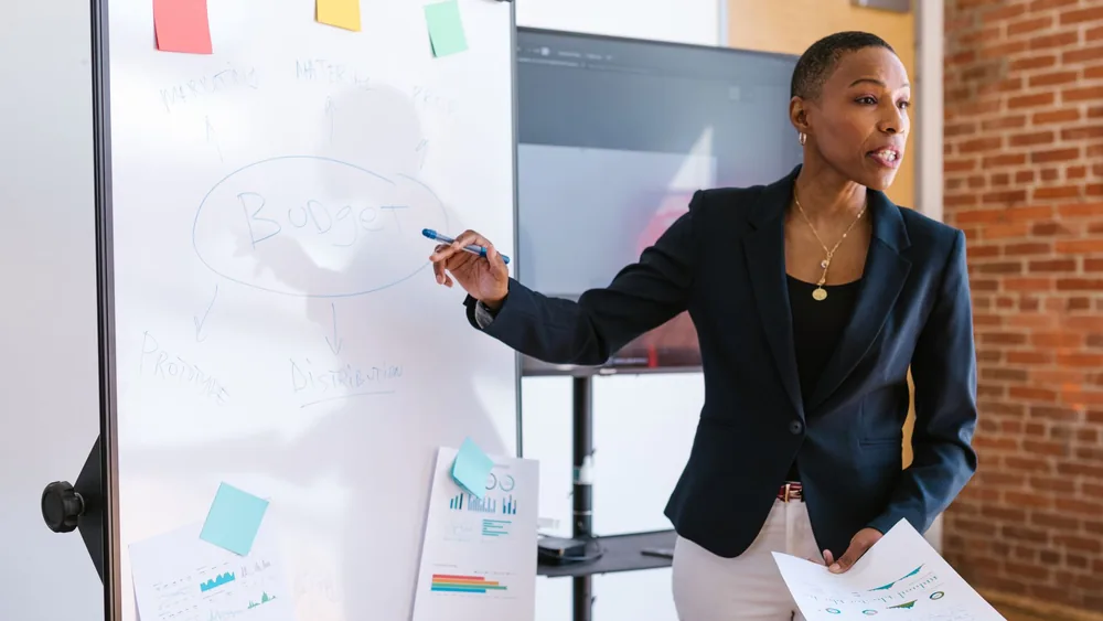 Professional businesswoman explaining budget strategy on a whiteboard during a meeting.