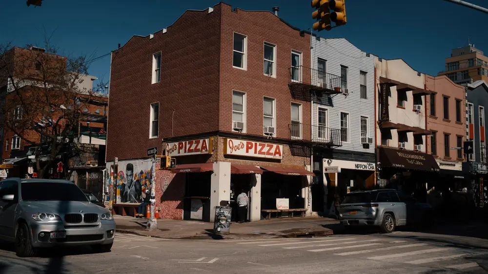 Street view of Joe's Pizza on a sunny day in Brooklyn, showcasing the lively urban atmosphere.