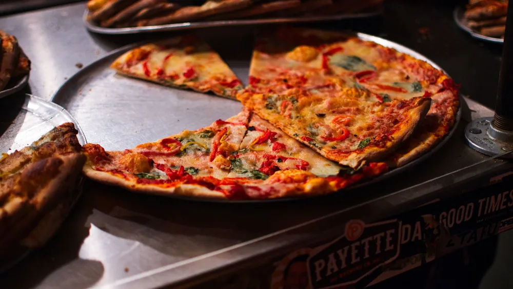 A mouth-watering view of vegetarian pizza slices with toppings on a metal tray, ready to serve.