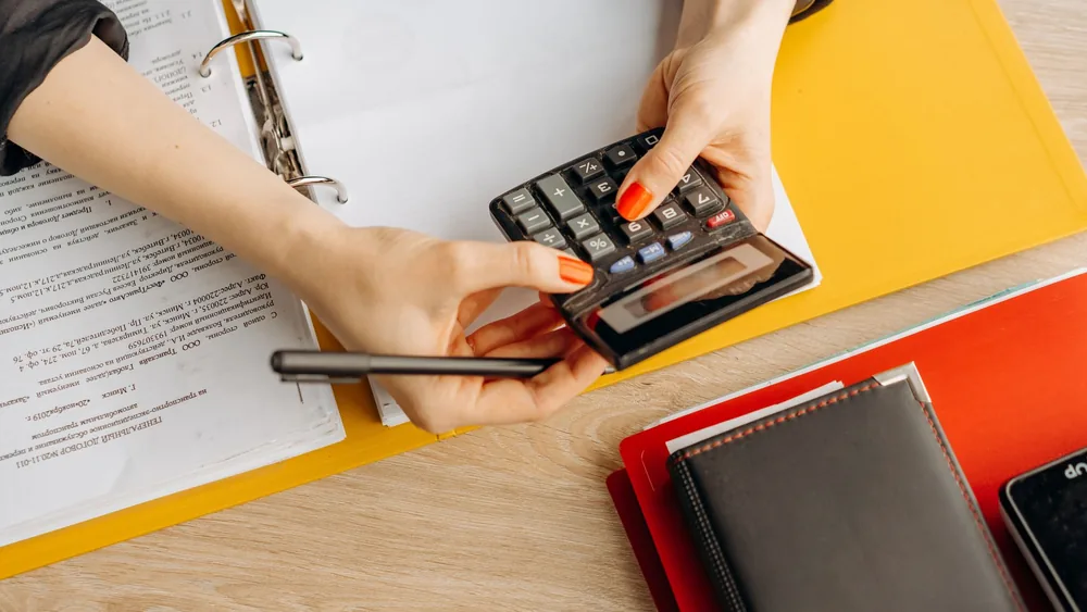 Hands using a calculator at a desk with documents and folders, ideal for finance or accounting themes.
