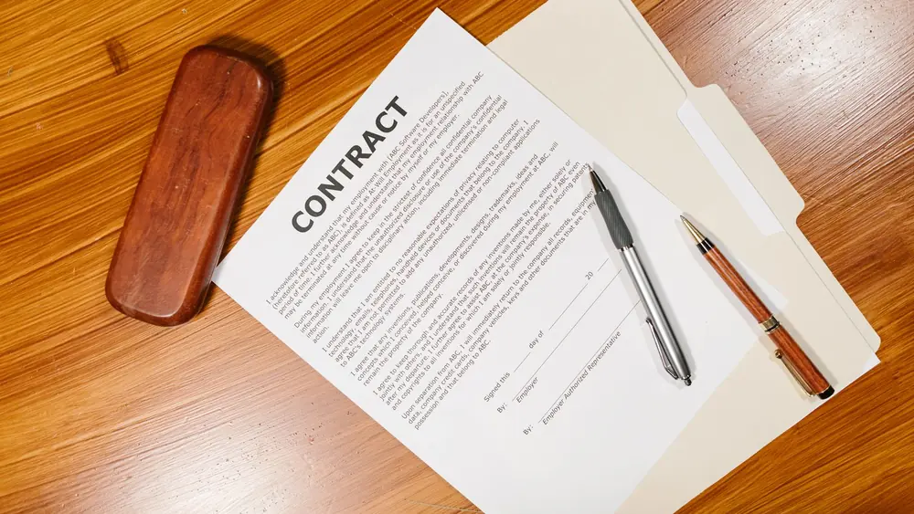 High-angle view of a contract document with pens and a case on a wooden table.