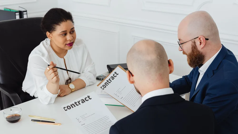 Three business professionals in discussion over a contract in a modern office setting.