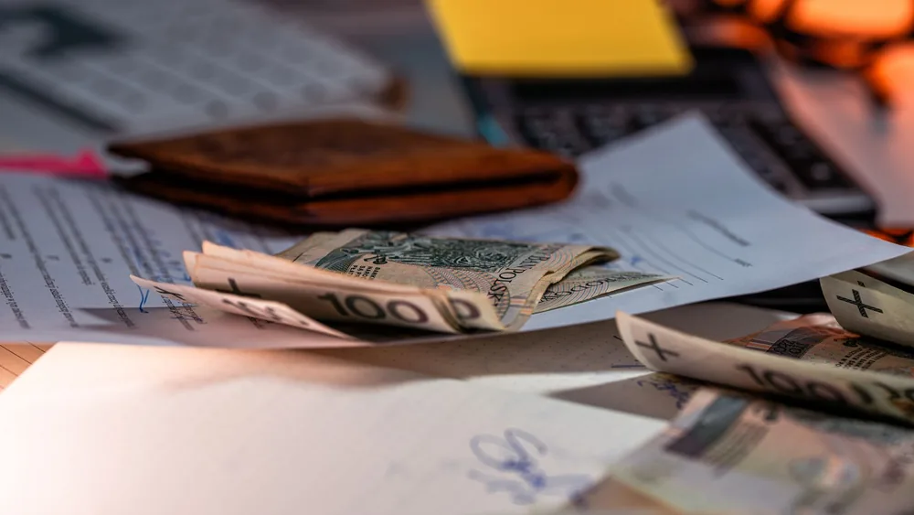 Zloty banknotes and financial paperwork scattered on a desk, representing budgeting and finance.