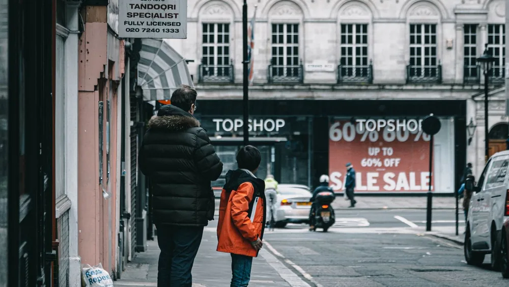 Father and son waiting on a London sidewalk near Strand Restaurant and Topshop signage.