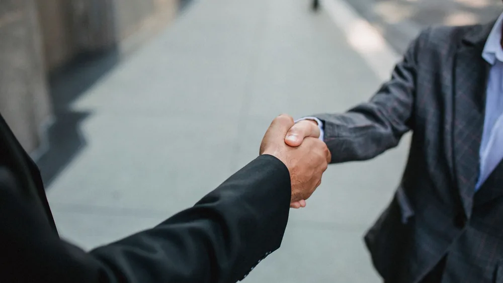 Close-up of two businessmen shaking hands outside, symbolizing partnership and agreement.