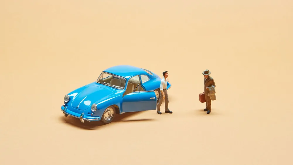 A miniature blue vintage car with two figurines on a beige background, perfect for modeling or creative projects.
