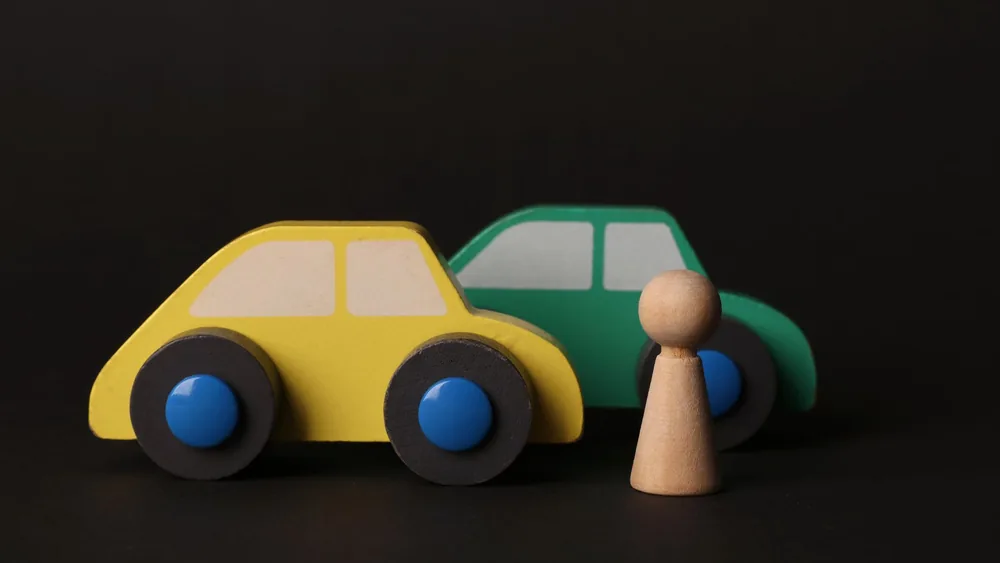 Close-up of colorful wooden toy cars and a peg figure on black background.