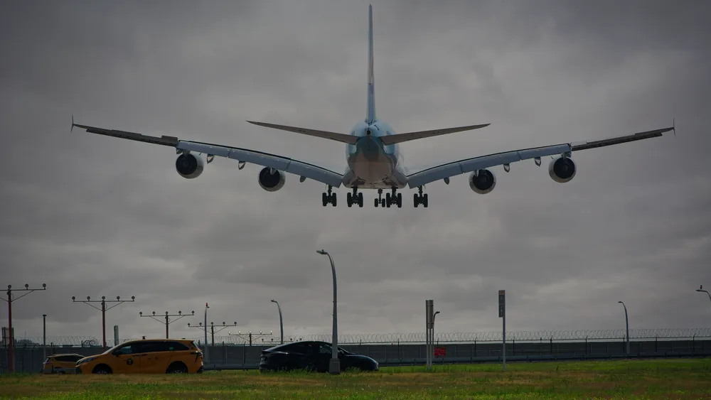 A passenger airplane lands at New York airport with cloudy skies, showcasing aviation and urban transport.