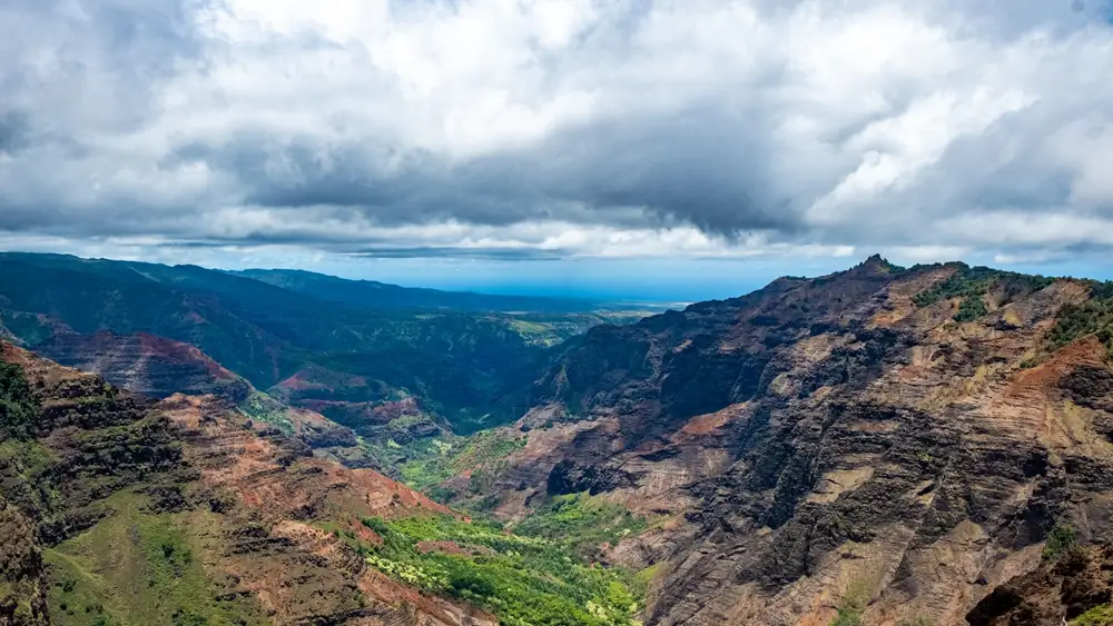 Stunning landscape view of Waimea Canyon, showcasing lush greenery and dramatic red cliffs under a cloudy sky.