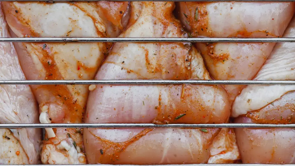 From above of closeup of raw chicken legs with seasoning cooking on metal grill grate