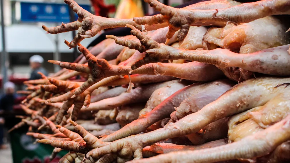 A close-up of chicken feet displayed for sale in a bustling wet market environment.