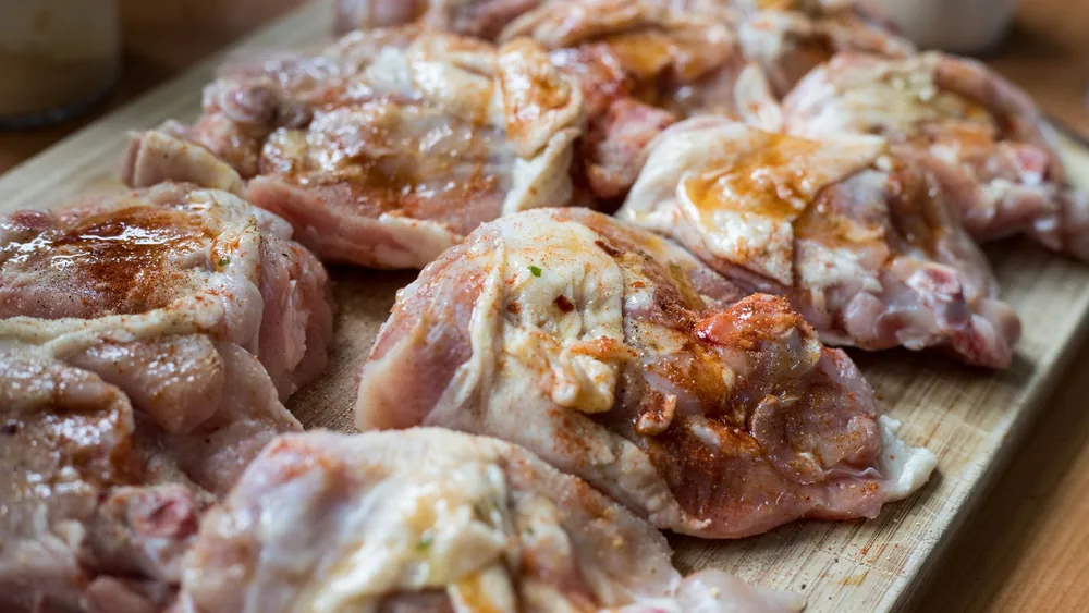 Raw chicken pieces seasoned with spices on a wooden board, ready for cooking.