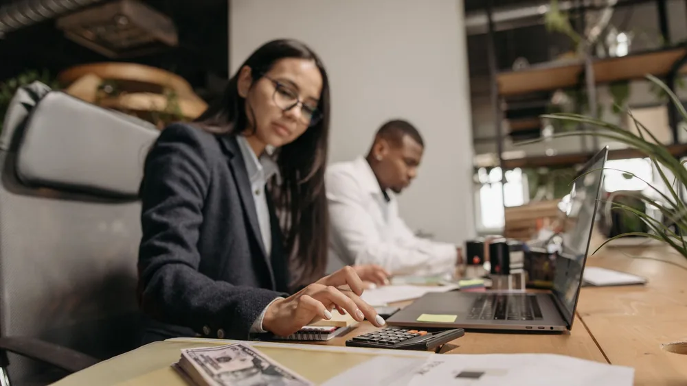 Two business professionals collaborating with a laptop and calculator in a modern office.