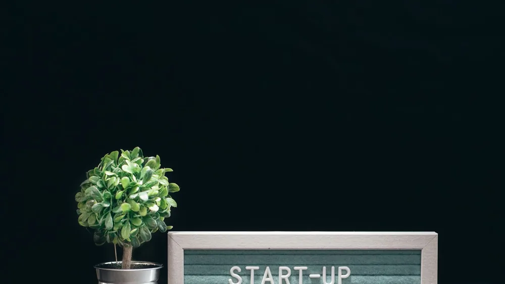 A modern close-up of a start-up theme with a potted plant and text board on a black background.