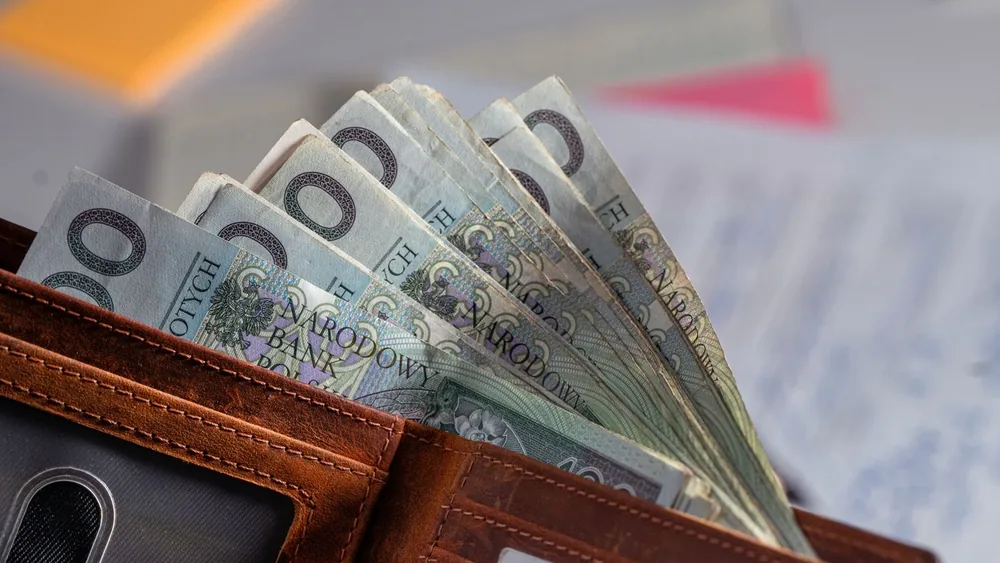 Brown leather wallet containing Polish zloty banknotes on cluttered desk
