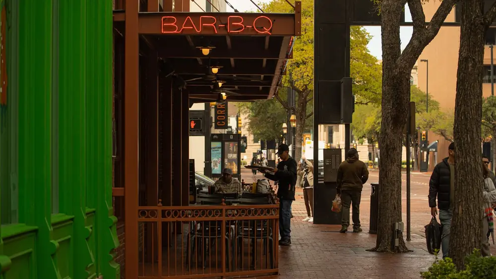 Downtown street with BAR-B-Q sign and people enjoying a city vibe.