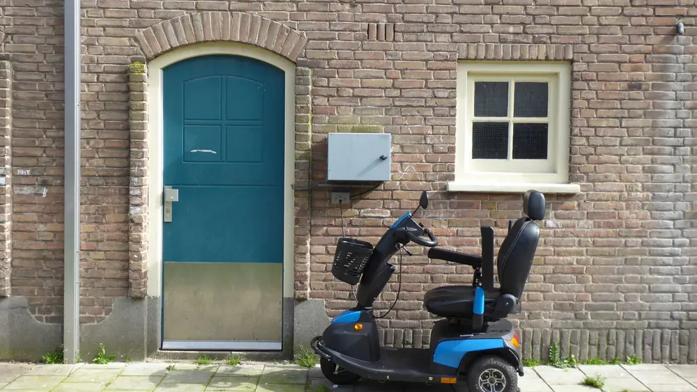 A blue mobility scooter parked beside a brick wall with a door in Amsterdam.