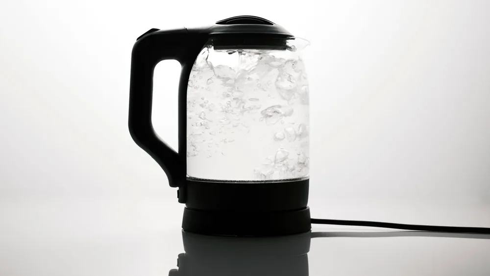 A sleek electric kettle boiling water, captured on a reflective white surface.