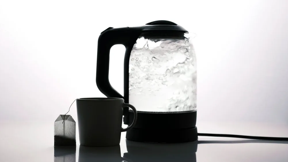 Silhouette of an electric kettle and a tea cup with a tea bag on a white background.