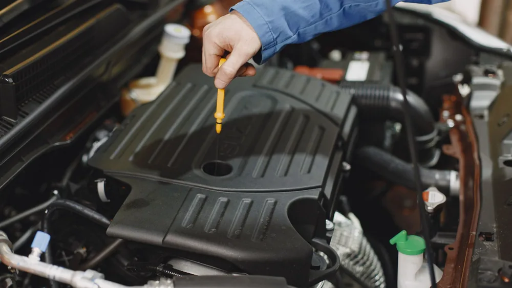 Close-up of a person checking engine oil using a dipstick in a car's engine bay.