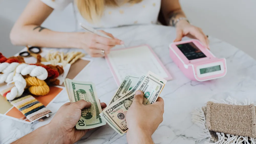 Two people handling cash and budgeting with a calculator and notebook at a table.