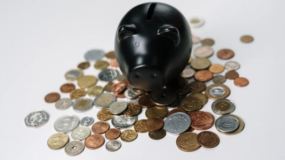 Black piggy bank surrounded by a variety of coins on a white surface, symbolizing savings and finance.