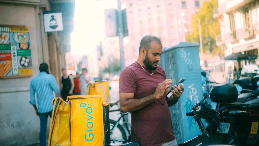 Delivery courier using his phone next to bicycle in a sunny urban street.