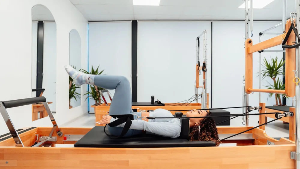 A woman performing fitness exercises on a Pilates reformer in a modern gym setting.