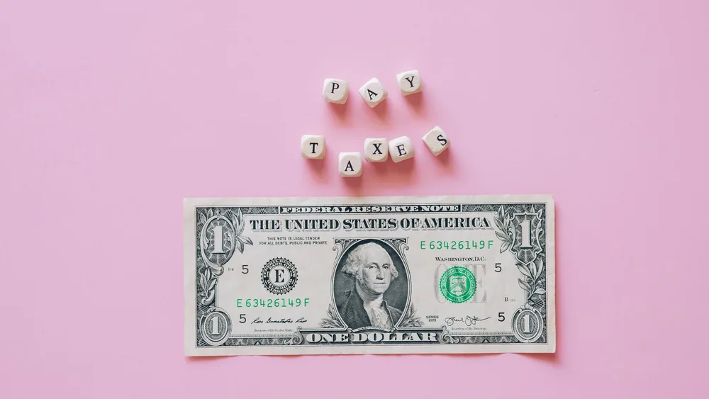 US one dollar bill on a pink background with pay taxes reminder cubes.