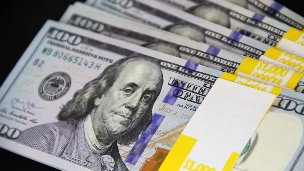 Close-up of stacked US hundred dollar bills on black surface, emphasizing wealth and finance.