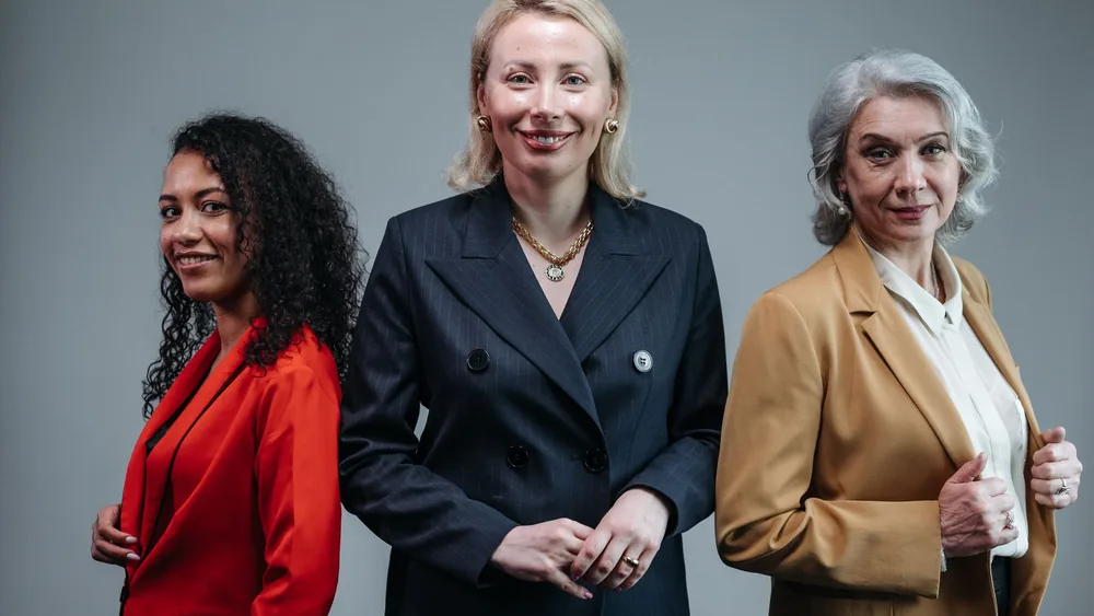 Three confident business women standing in fashionable attire, exuding professionalism.