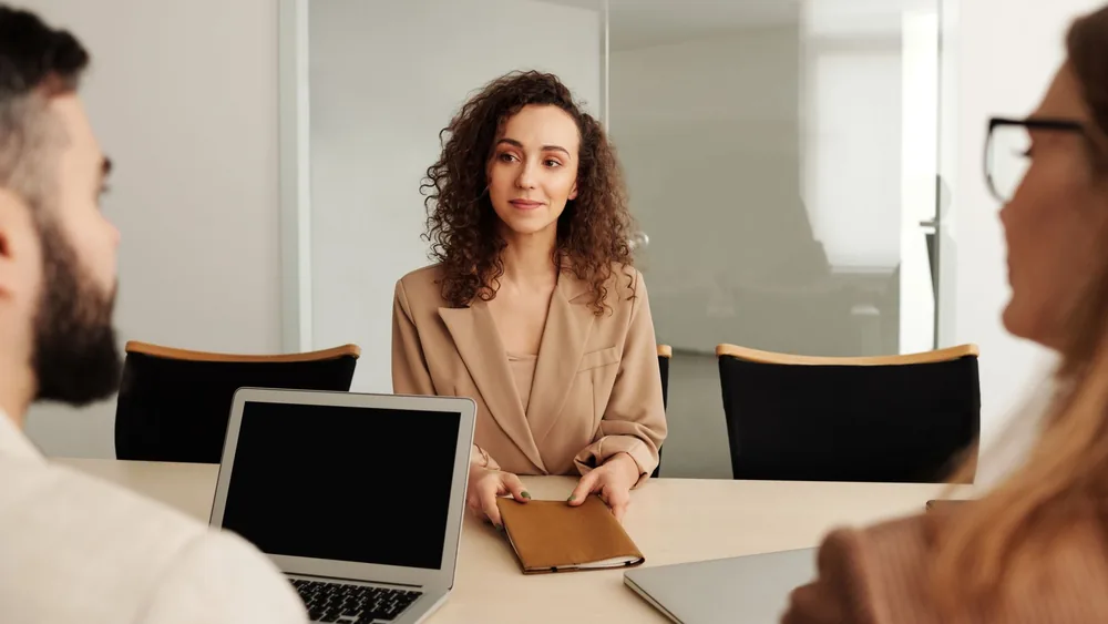 A woman in a business suit participates in a job interview, showcasing professionalism and modern office environment.