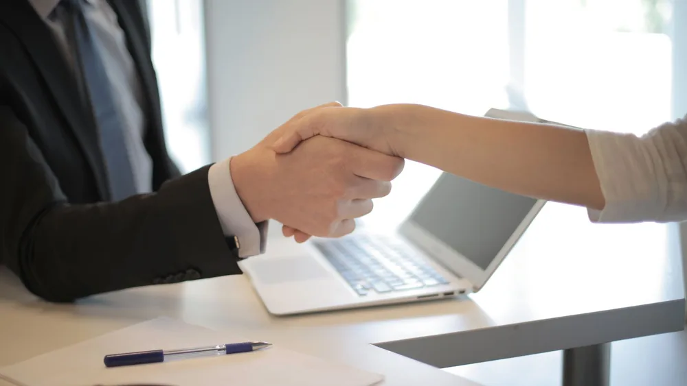 Close-up of a professional handshake over a laptop during a business meeting in an office.