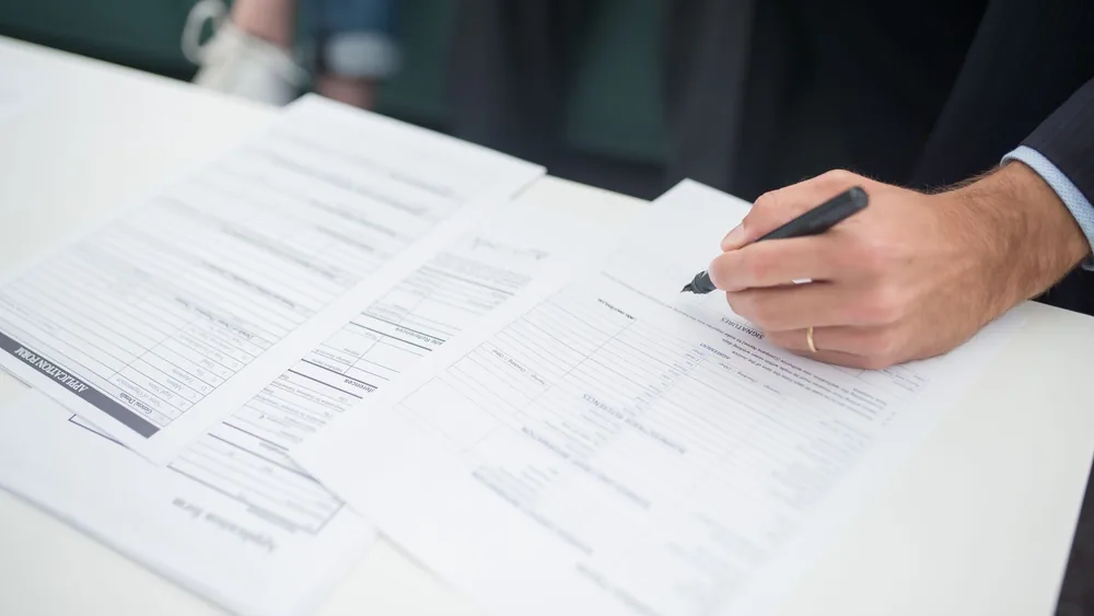 Close-up of a hand signing insurance documents in an office setting.